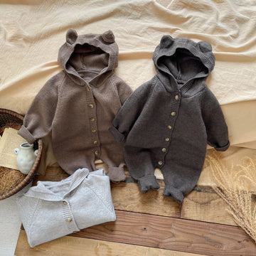 Two baby rompers on a wooden surface with a neutral background