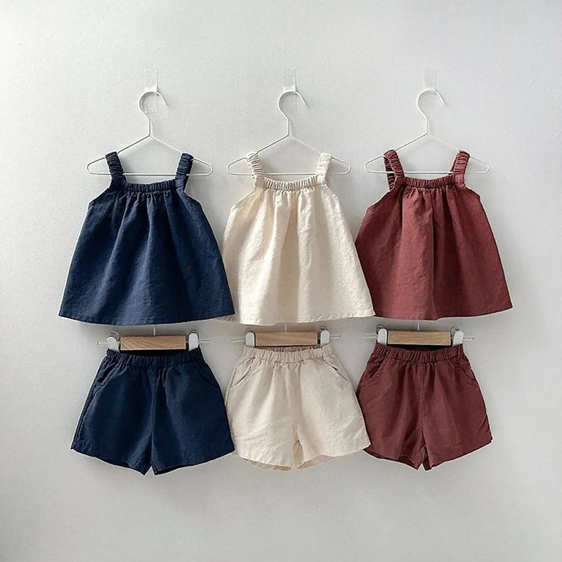 Set of children's clothing including dresses and shorts on hangers against a white background