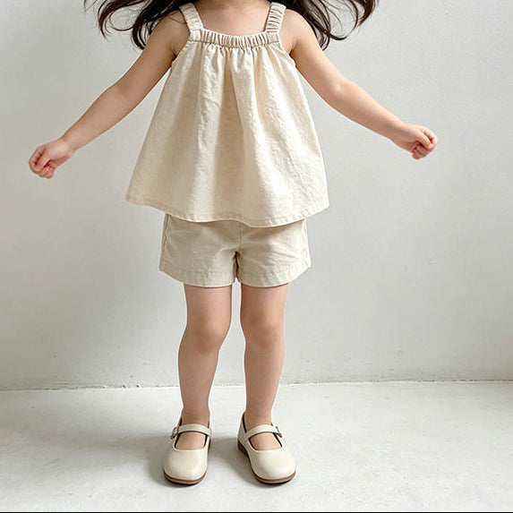 Set of children's clothing including dresses and shorts on hangers against a white background