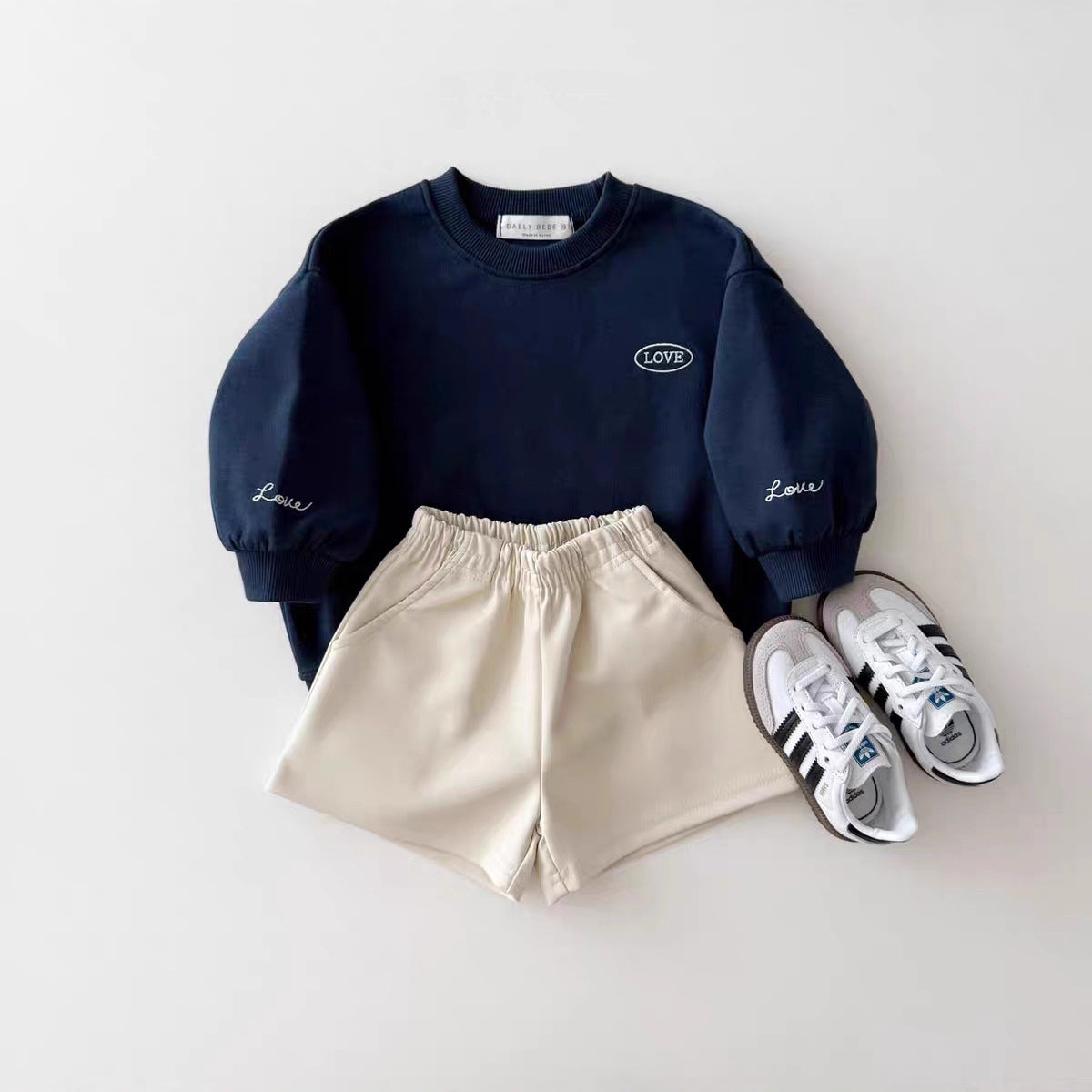Navy sweatshirt, beige shorts, and white sneakers on a light gray background