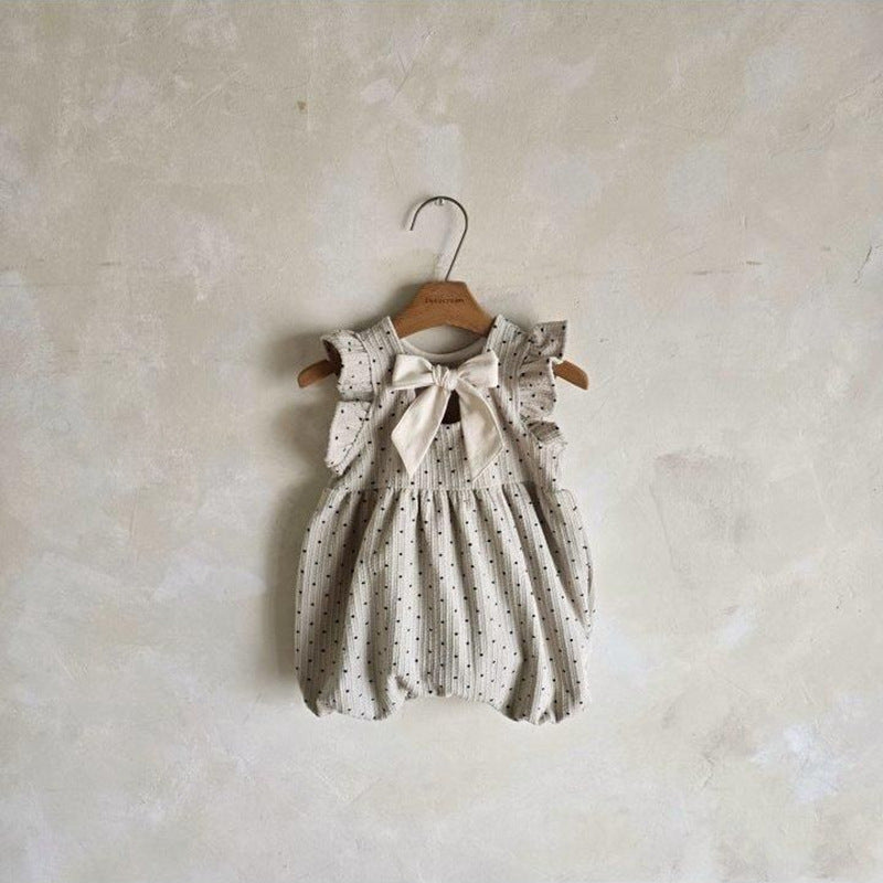 Two baby rompers on hangers against a plain wall.