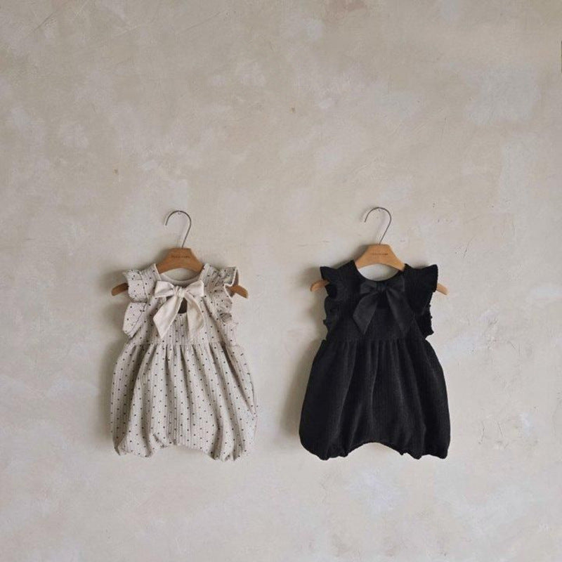 Two baby rompers on hangers against a plain wall.
