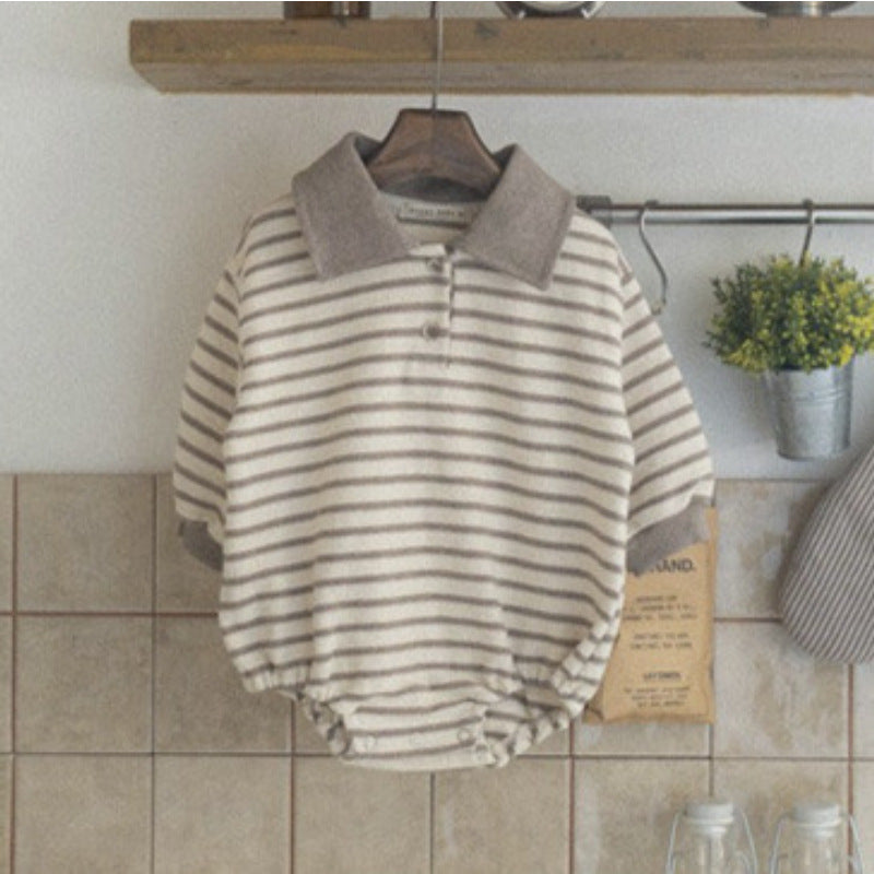 Striped baby romper hanging on a wooden hanger against a tiled wall.