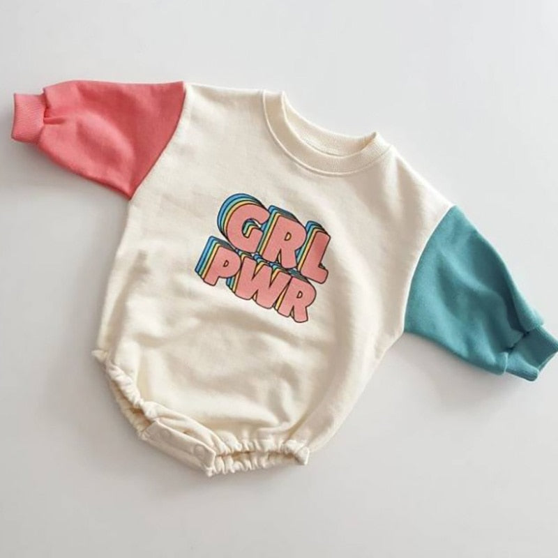 A 'GRL PWR' bodysuit with color-blocked sleeves in pink and blue on a beige background with the text 'GRL PWR' on the front.