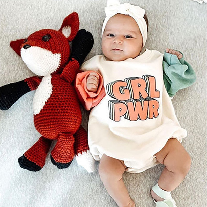 A 'GRL PWR' bodysuit with color-blocked sleeves in pink and blue on a beige background with the text 'GRL PWR' on the front.